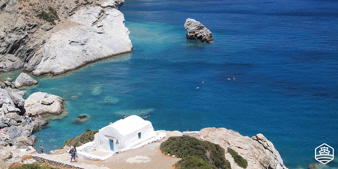 Die Kirche von Agia Anna und Menschen, die in der gleichnamigen Felsenbucht schwimmen