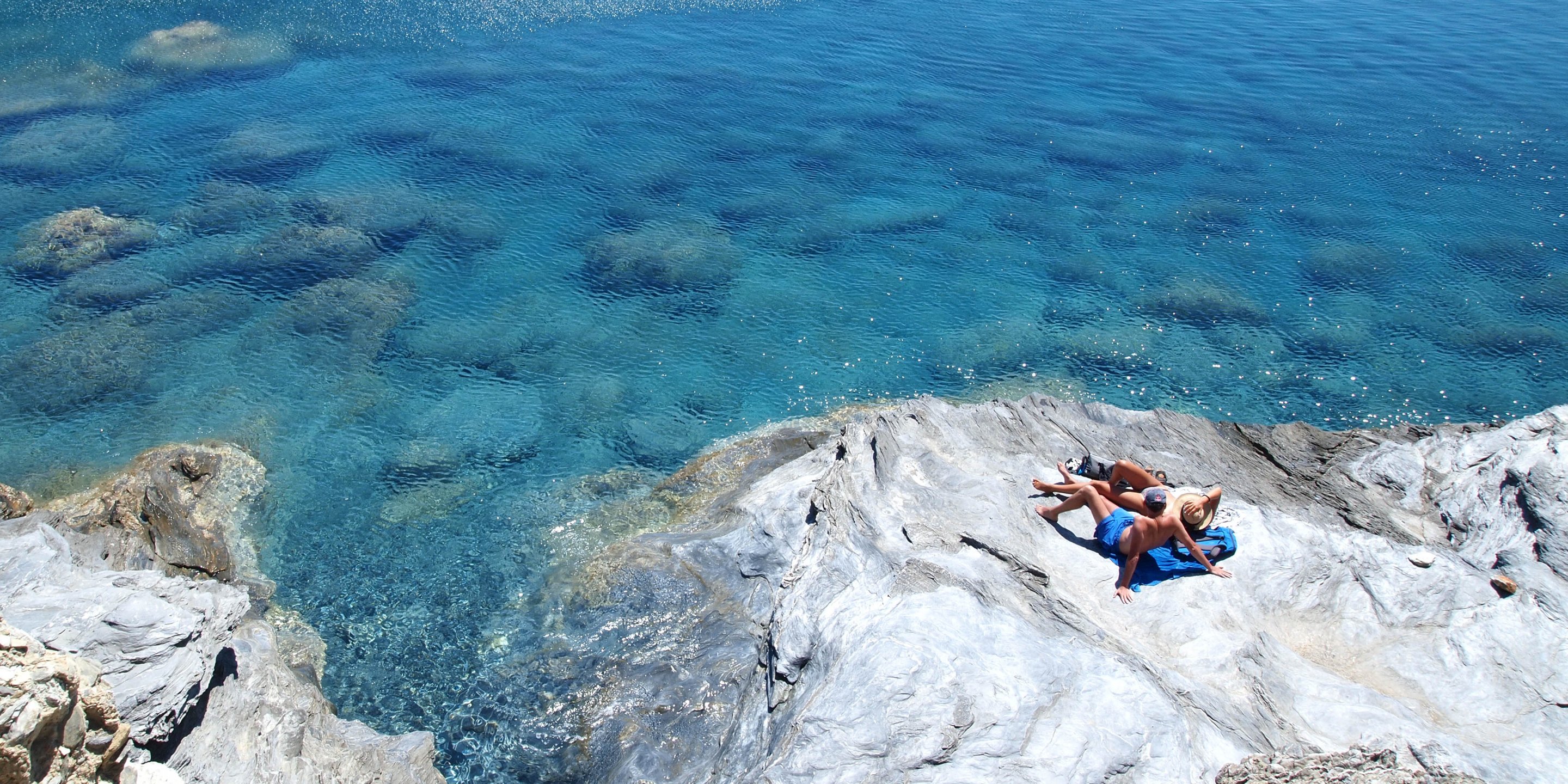 A couple enjoy the sun on a rock next to the beach of Mouros, in Amorgos
